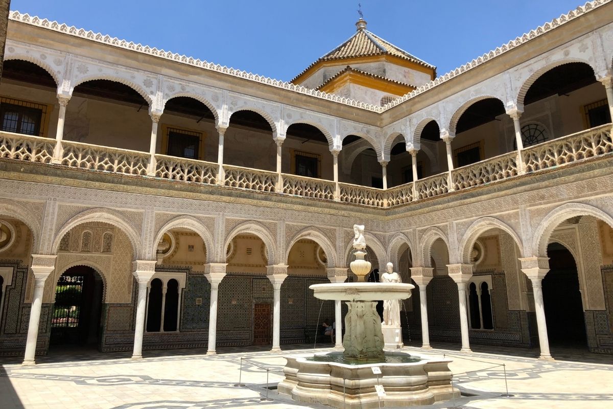 Pátio interior de uma casa típica de Andaluzia, com uma fonte de água ao centro e detalhes em arabesco e em mosaico.