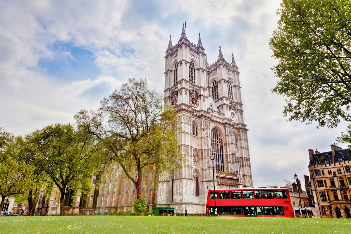 Fachada da Abadia de Westminster com suas duas torres imponentes e um ônibus de dois andares vermelho passando a sua frente