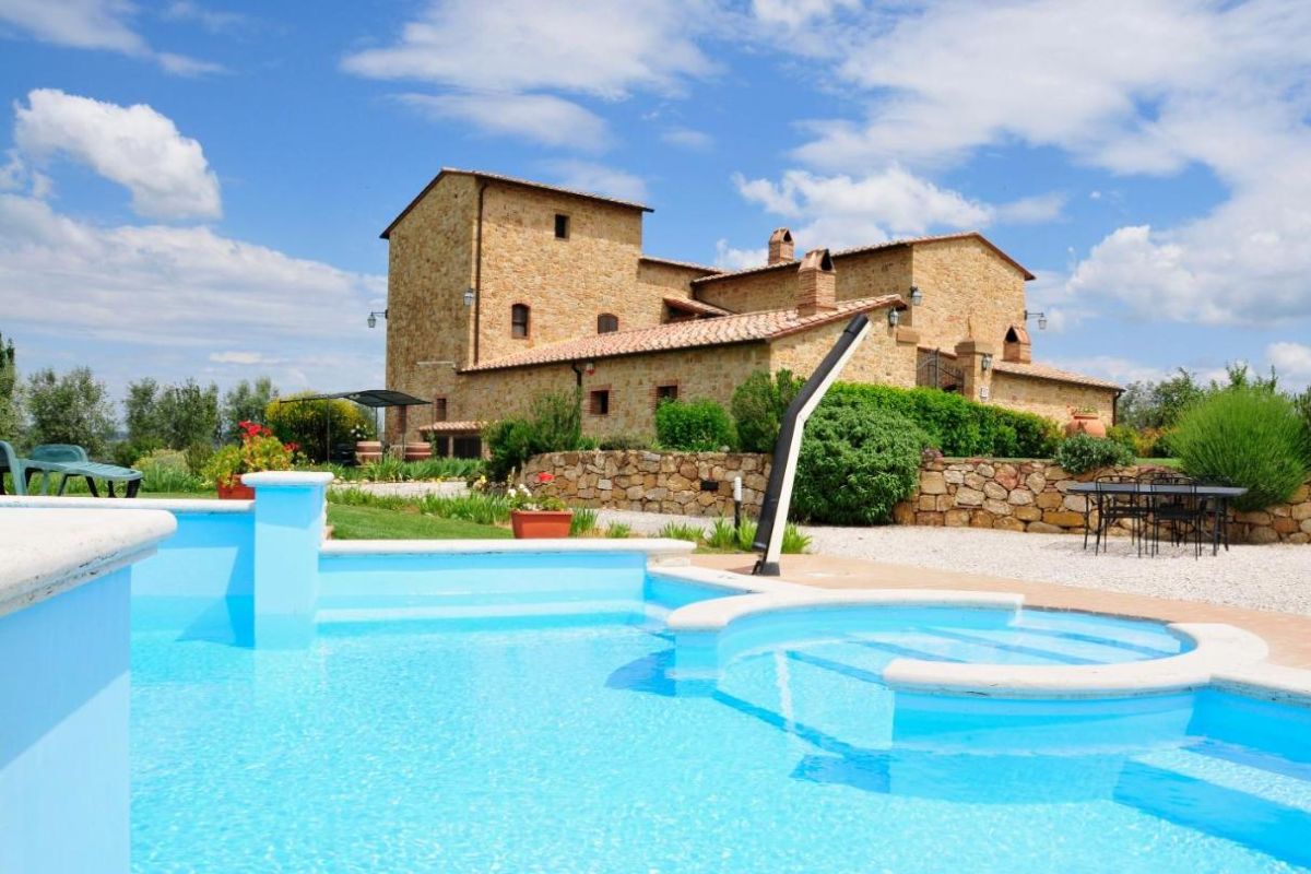 Hospedagem Il Macchione no Val d'Orcia, Itália, em contrução medieval em pedras ao fundo e grande piscina em primeiro plano