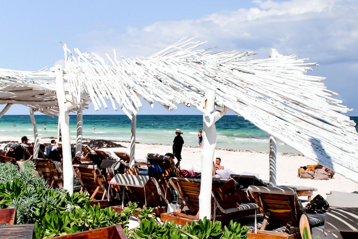 Quioesque de praia com cadeiras e espreguiçadeiras na areia de Tulum com mar azul turquesa ao fundo