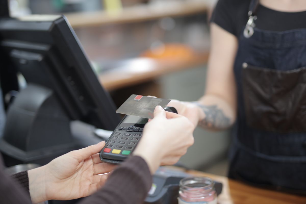 Pessoa fazendo um pagamento com cartão de crédito por aproximação em uma maquinina de cartão.