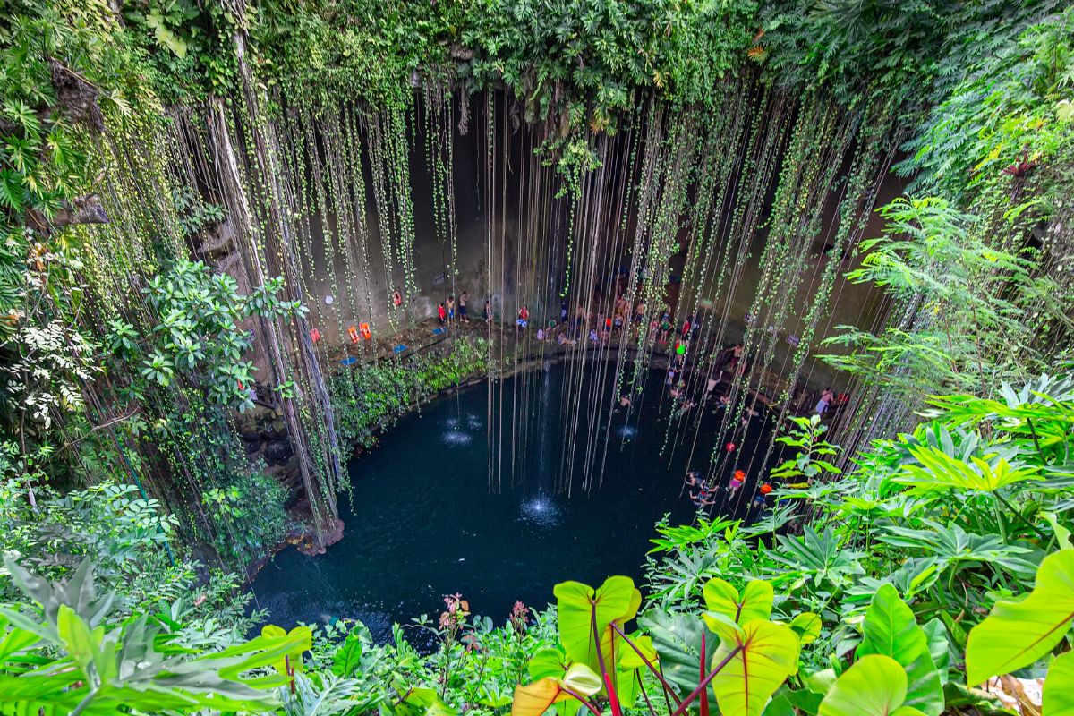 Piscina natural de água doce em formato oval rodeada por alto penhasco e por natureza exuberante e verde