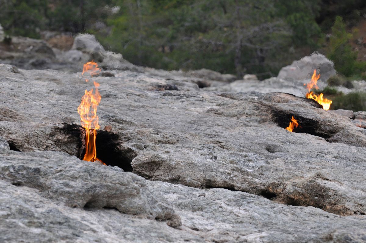 Pequenas chamas de fogo saindo de pedras em meio à natureza