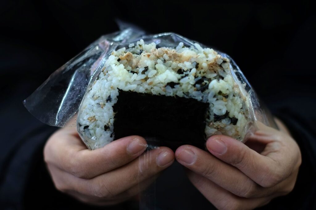 Homem segurando um onigiri, bolinho de arroz típico do Japão encontrado nas lojas de conveniência