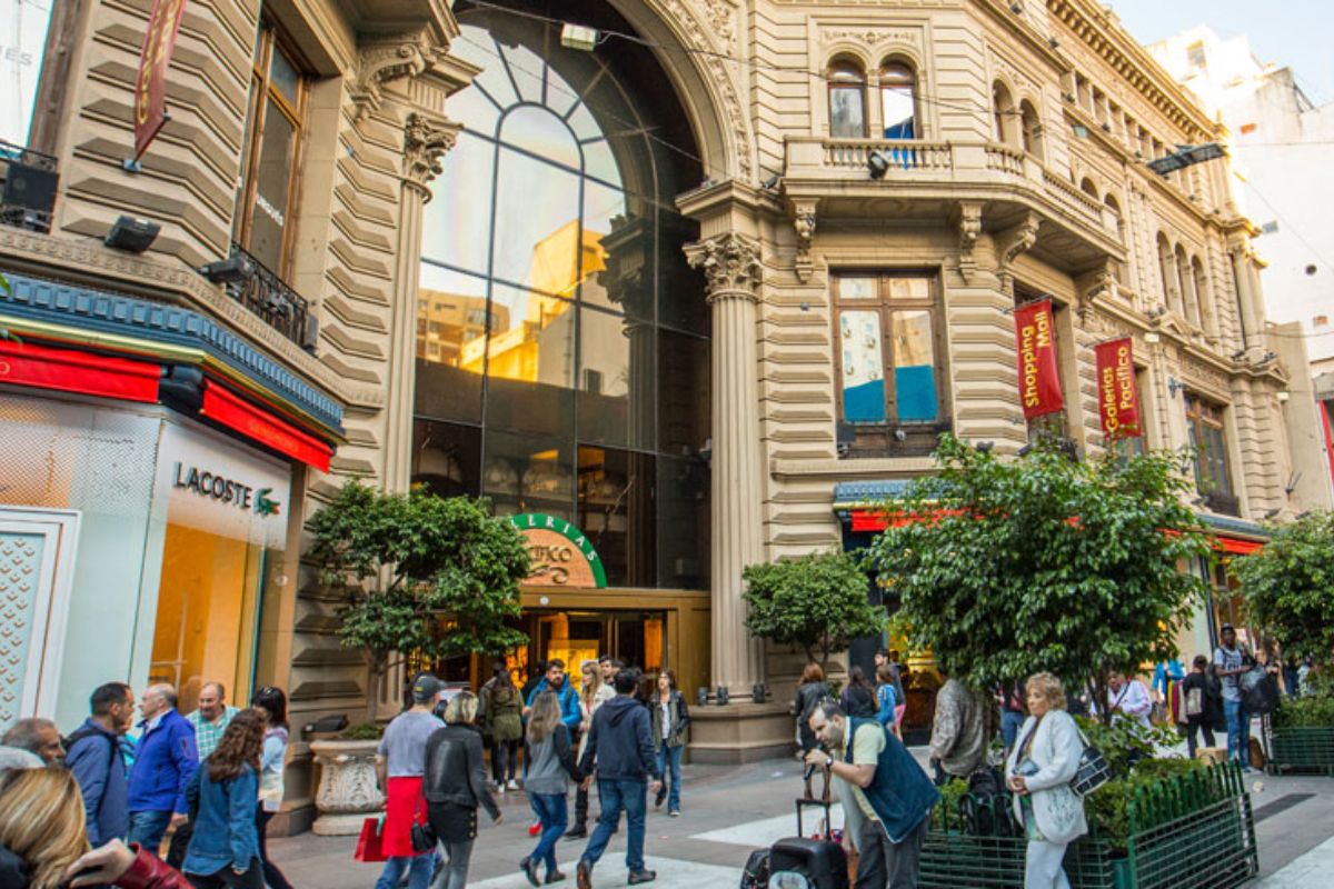 Entrada da Galerias Pacífico, na Calle Florida, em Buenos Aires, com grande movimento de pessoas ao redor e vitrines de lojas de marca