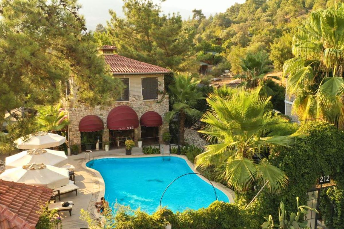 Hotel em Olympos, na Turquia, com piscina, espreguiçadeiras, muitas árvores e casa de pedras de dois andares ao fundo