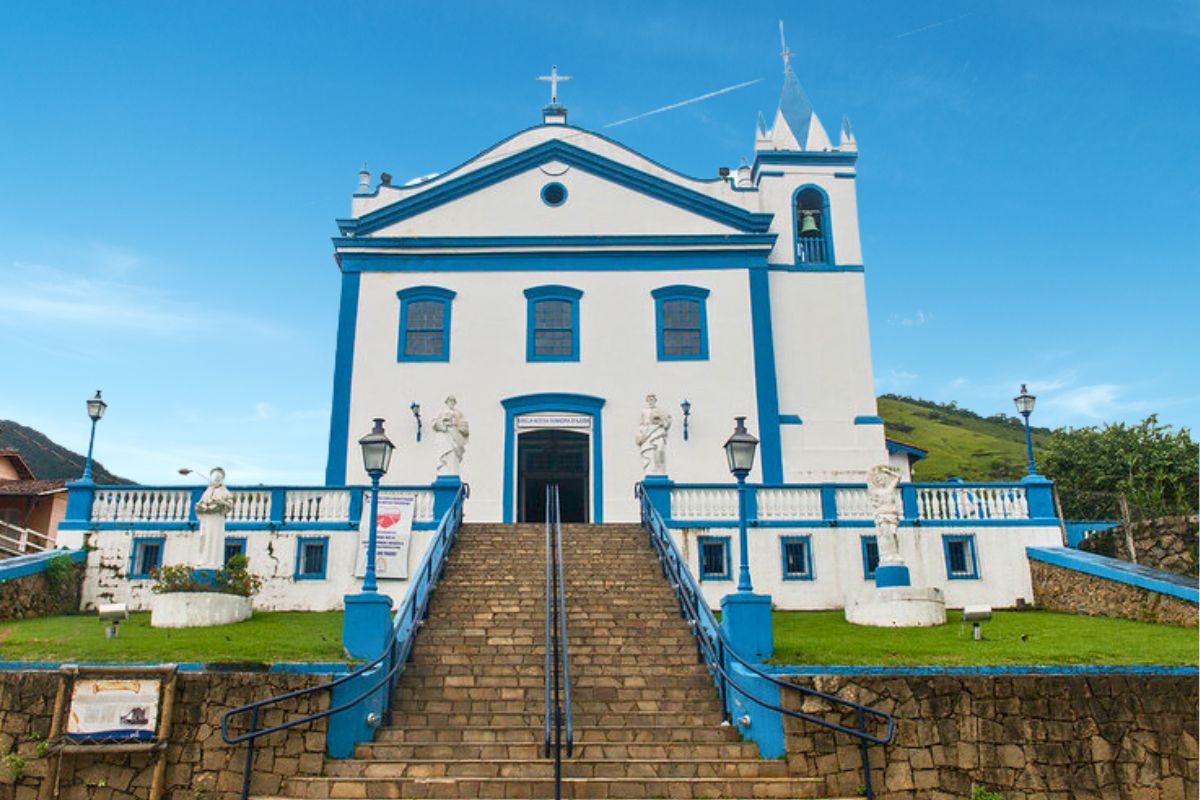 Faixada de igreja de arquitetura colonial em Ilhabela com grande escadaria na entrada e paredes pintadas em branco com detalhes em azul