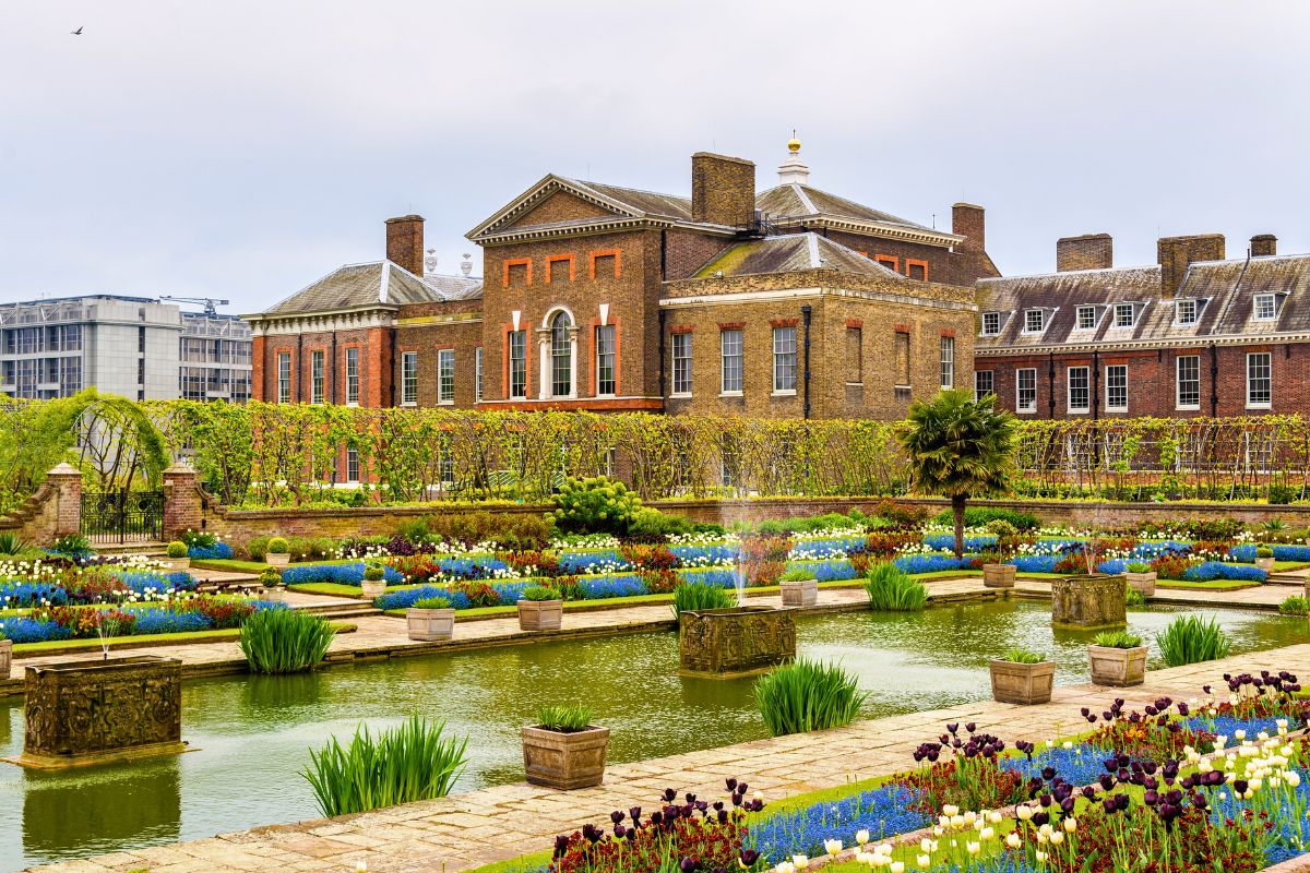 Palácio de Kensington construído em tijolos aparentes com grande jardim a sua frente, com flores e lago artificial