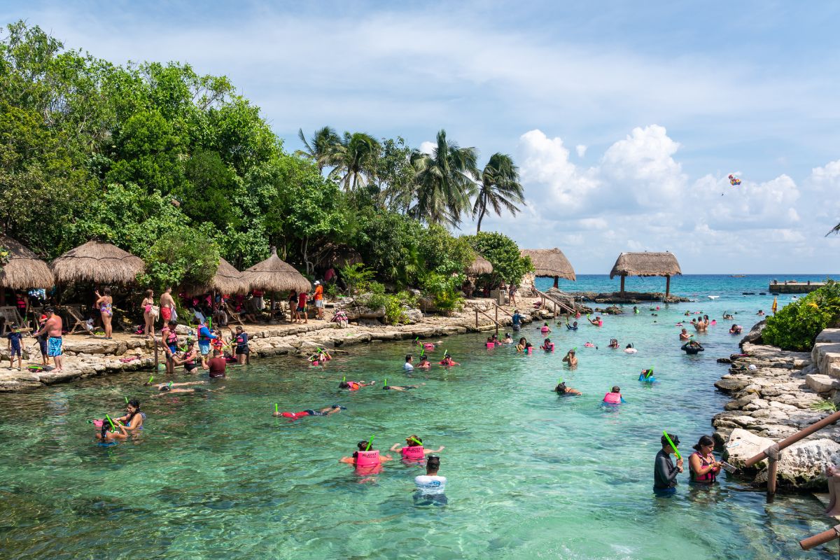 Grande piscina natural rodeada por natureza, com pessoas praticando snorkel e mar ao fundo