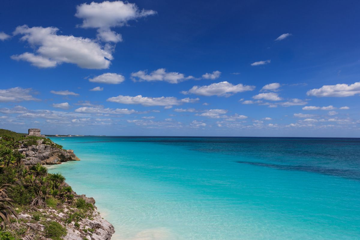 Praia de Tulum, no México, com mar calmo, água de cor azul turquesa e ruina maia ao fundo