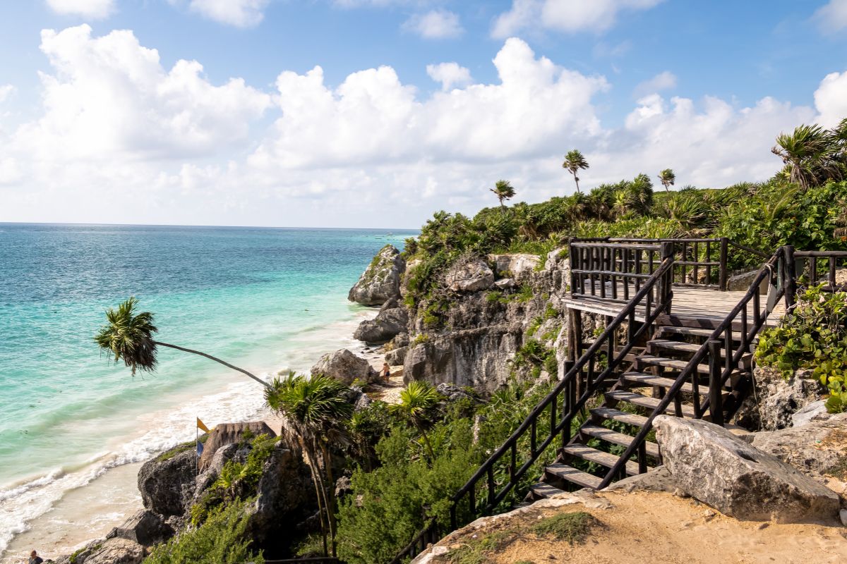 Escadaria em madeira que liga falésia onde estão as ruínas maias de Tulum com a praia de mar azul turquesa