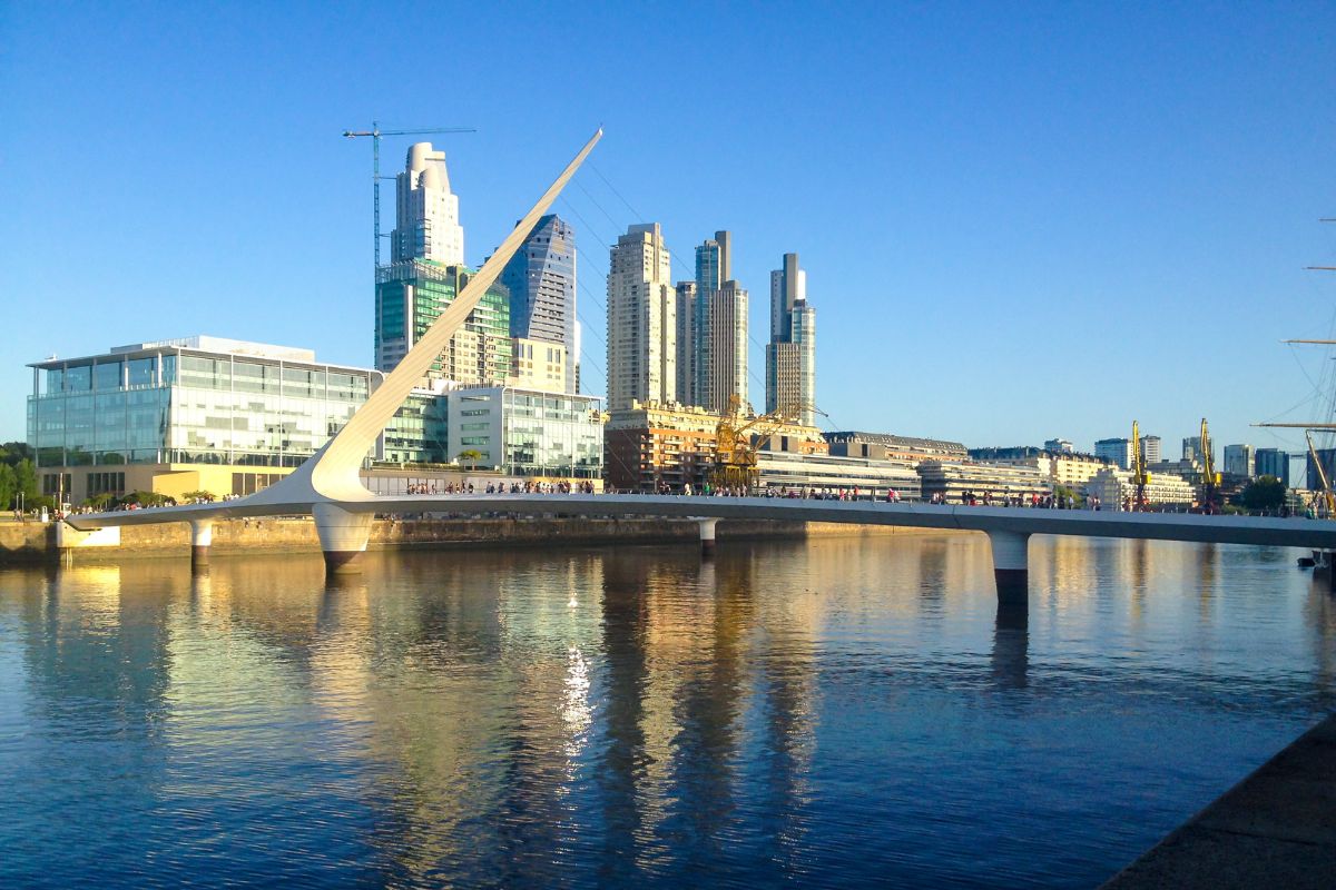 Ponte das Mulheres, localizada no bairro de Puerto Madero, em Buenos Aires, com prédios modernos e espelhados no horizonte