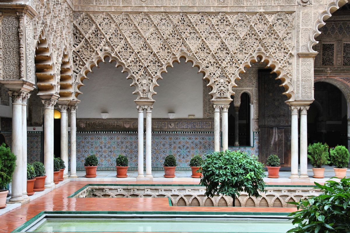 Pátio interno do Palácio de Real Alcázar, em Sevilha, com espelhos d'água e decoração em arabescos e mosaicos.