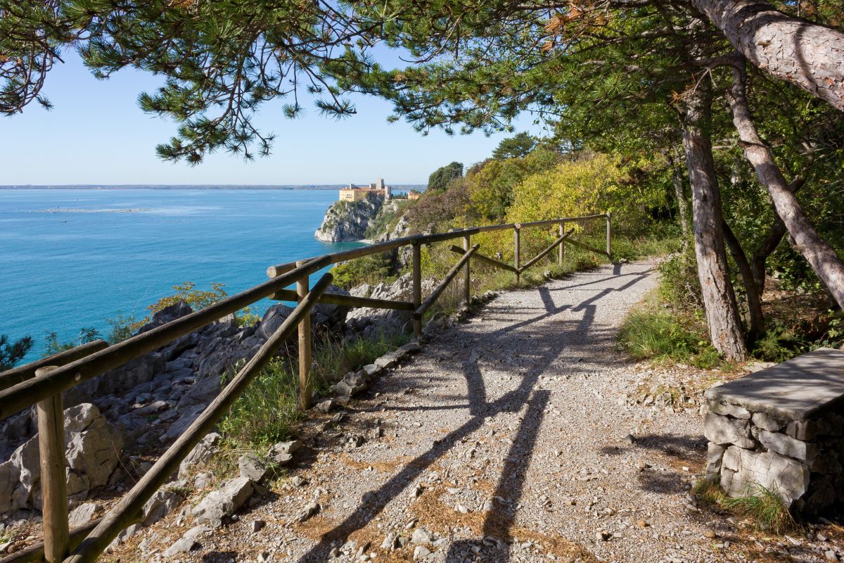 Trilha no entorno do mar de Trieste com castelo ao fundo