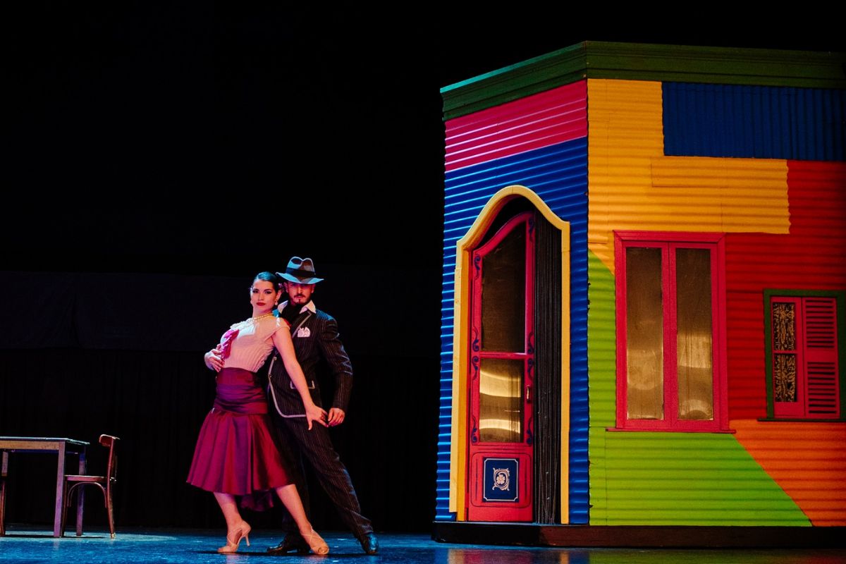 Cena de um show de tango com casal de bailarinos e cenário do bairro Caminito de Buenos Aires ao fundo